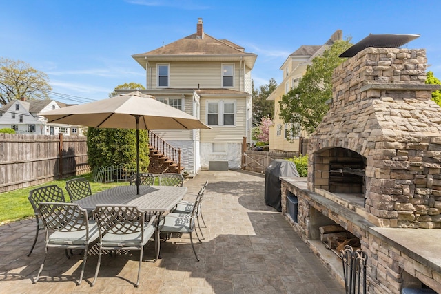 view of patio / terrace featuring a fenced backyard, outdoor dining space, a grill, and an outdoor stone fireplace