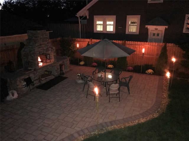 patio at twilight featuring fence and an outdoor stone fireplace