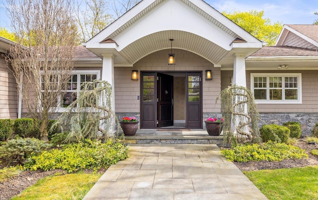 property entrance featuring a porch, roof with shingles, and stone siding