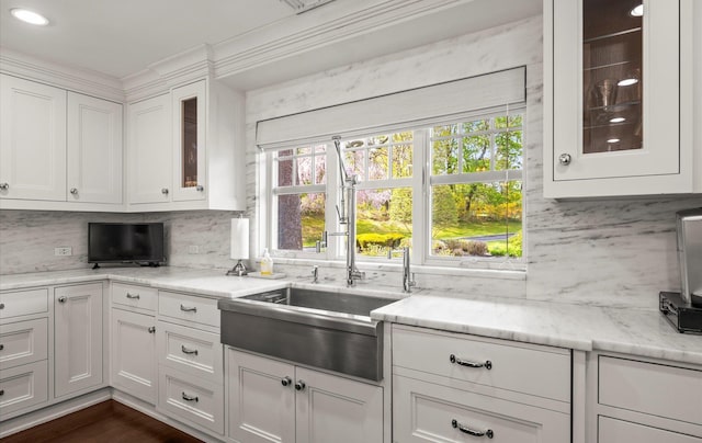 kitchen featuring decorative backsplash, light stone countertops, a sink, white cabinets, and glass insert cabinets