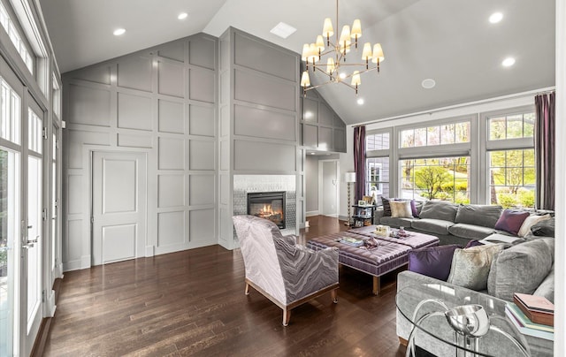 living area with an inviting chandelier, dark wood finished floors, high vaulted ceiling, a glass covered fireplace, and a decorative wall