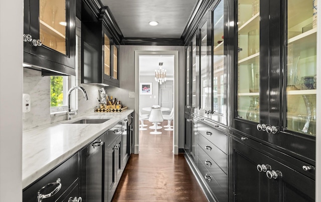 kitchen with light stone countertops, a sink, dark cabinetry, dark wood finished floors, and ornamental molding