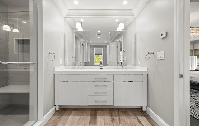 full bath featuring double vanity, crown molding, wood finished floors, a sink, and baseboards