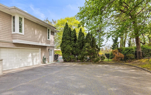 view of side of property featuring an attached garage, fence, and driveway