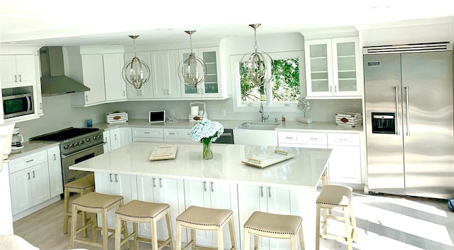 kitchen with light countertops, built in appliances, wall chimney range hood, and glass insert cabinets