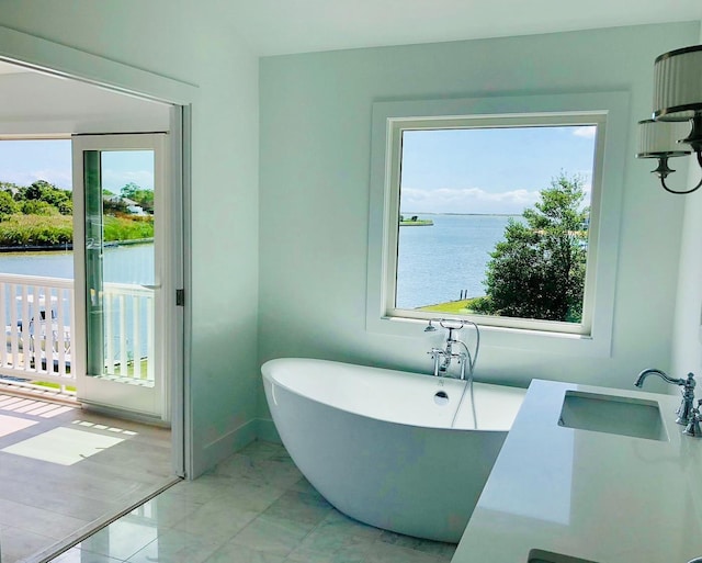bathroom with a freestanding bath, a sink, marble finish floor, baseboards, and a water view