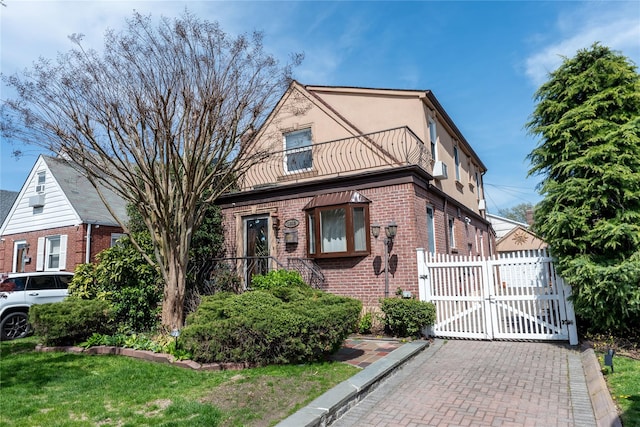 view of front of house with a gate, brick siding, fence, a balcony, and stucco siding