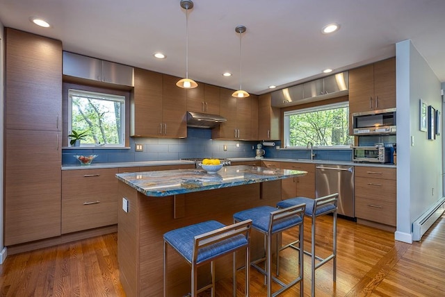 kitchen with modern cabinets, baseboard heating, a kitchen bar, under cabinet range hood, and stainless steel appliances