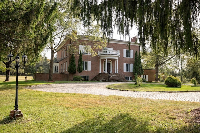 view of front facade with brick siding, a chimney, a balcony, and a front yard