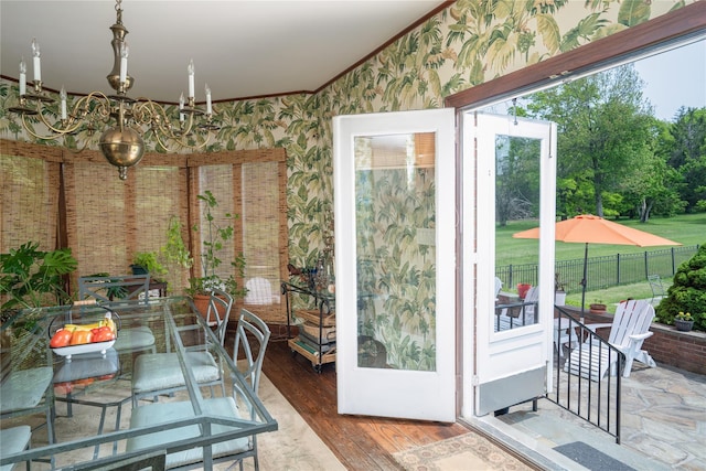 entryway with ornamental molding, wallpapered walls, wood finished floors, and a notable chandelier