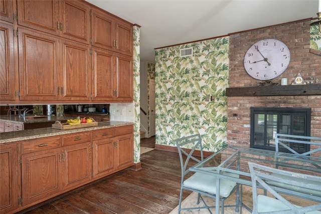 kitchen featuring a brick fireplace, visible vents, brown cabinetry, and dark wood-type flooring