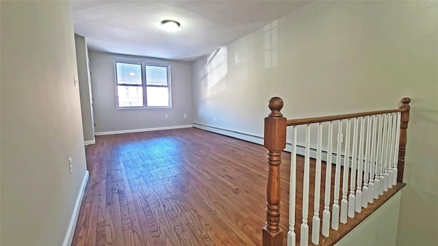 empty room with baseboards, a baseboard heating unit, and wood finished floors