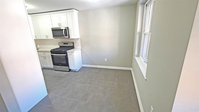 kitchen featuring white cabinets, appliances with stainless steel finishes, tile patterned flooring, light countertops, and baseboards