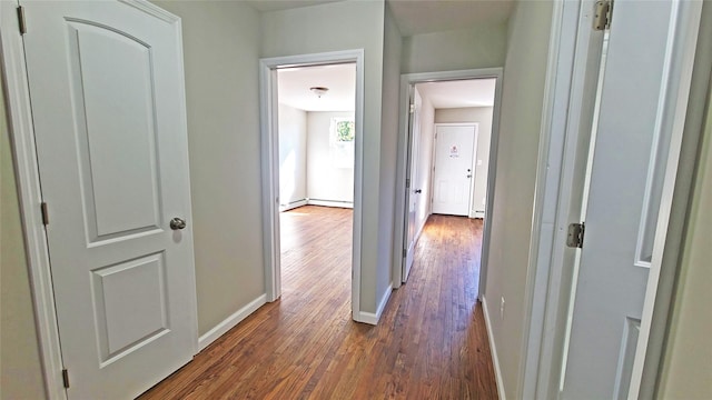 corridor featuring baseboards, baseboard heating, and dark wood finished floors