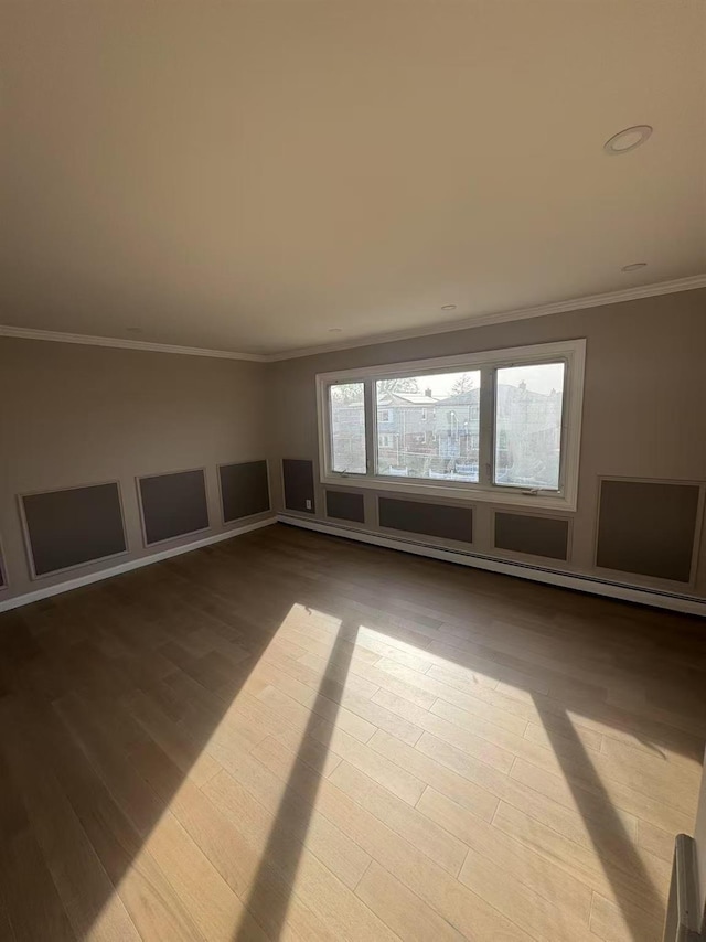 empty room featuring a baseboard heating unit, ornamental molding, and wood finished floors