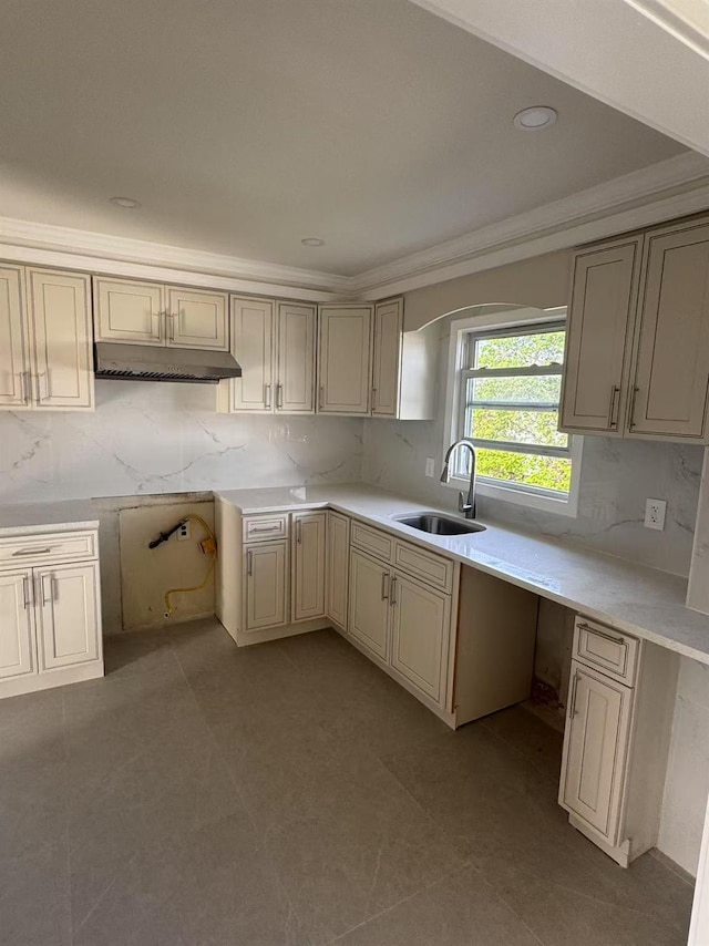 kitchen with backsplash, a sink, ornamental molding, under cabinet range hood, and cream cabinetry