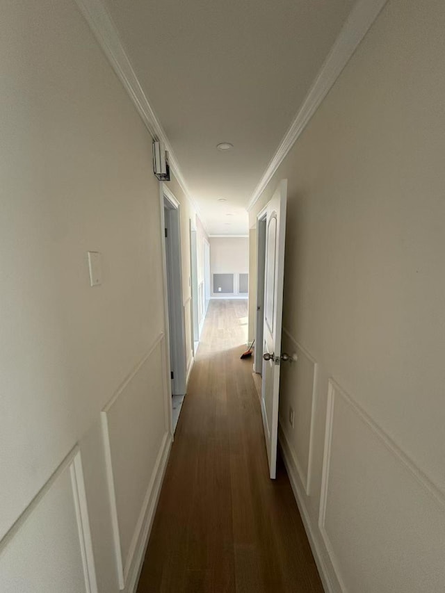 corridor with crown molding, dark wood finished floors, a decorative wall, and wainscoting
