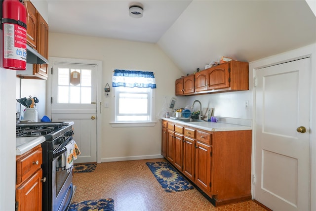 kitchen featuring lofted ceiling, stainless steel gas stove, light countertops, brown cabinets, and a sink