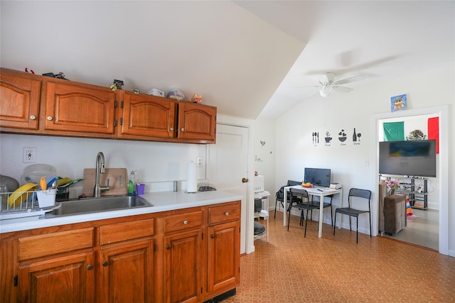 kitchen with ceiling fan, brown cabinetry, vaulted ceiling, a sink, and light countertops