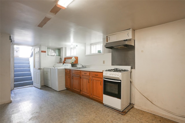 kitchen with washing machine and clothes dryer, gas range gas stove, a sink, light floors, and under cabinet range hood