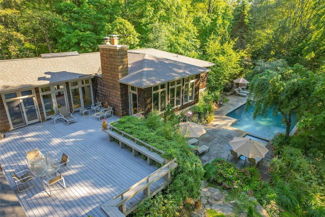 back of house featuring a wooden deck, an outdoor pool, a sunroom, a shingled roof, and outdoor dining space