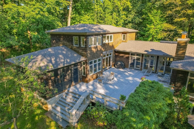 back of property with roof with shingles, a deck, a chimney, a forest view, and french doors