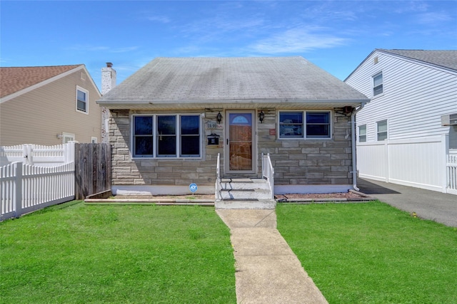 view of front facade with roof with shingles, a front yard, fence, and stone siding
