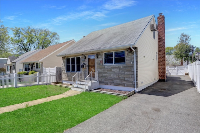 view of front of property featuring a front lawn, fence, stone siding, a chimney, and driveway