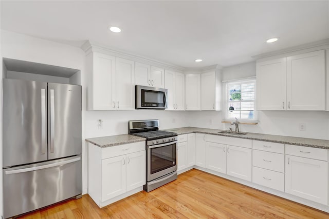 kitchen with white cabinets, stainless steel appliances, light stone countertops, and light wood-style floors