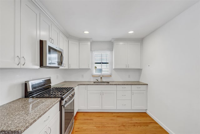 kitchen featuring light stone countertops, white cabinetry, a sink, stainless steel appliances, and light wood-style flooring