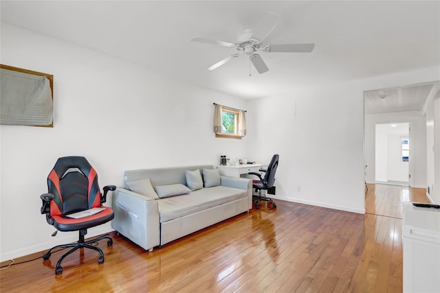 living area featuring a ceiling fan, baseboards, and hardwood / wood-style floors