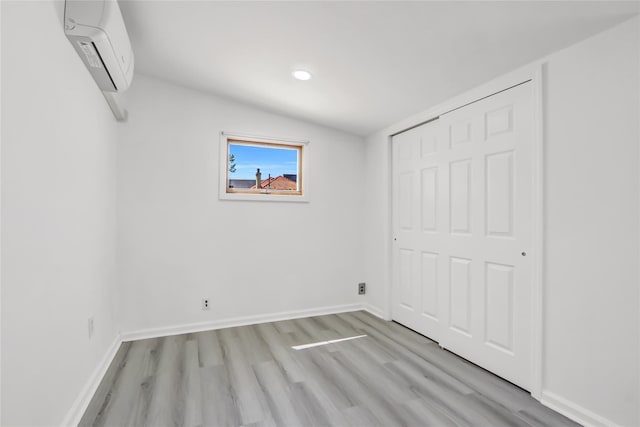 unfurnished bedroom with baseboards, vaulted ceiling, light wood-type flooring, a wall mounted AC, and a closet