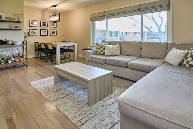 living area with baseboards, light wood finished floors, and a chandelier