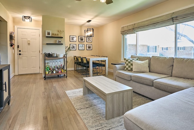 living room featuring baseboards, light wood-style flooring, and ceiling fan with notable chandelier