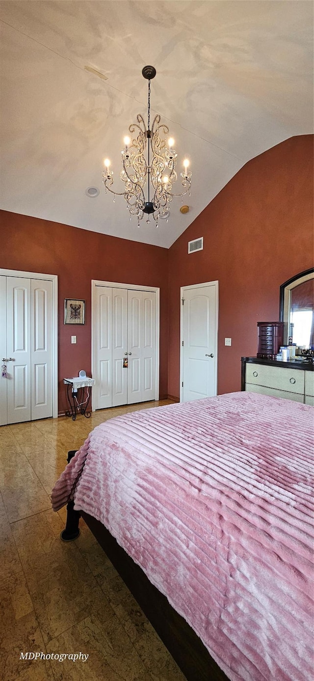 bedroom with visible vents, lofted ceiling, two closets, and a chandelier