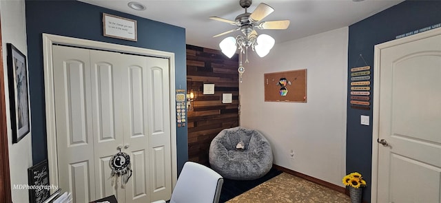 office area with baseboards, a ceiling fan, and wood walls