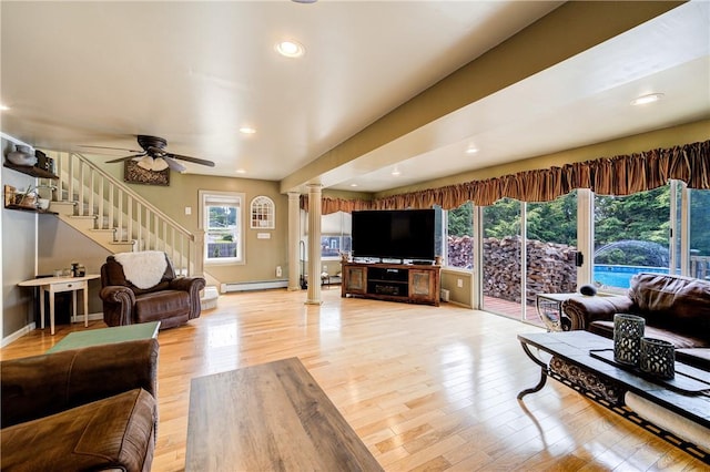 living room featuring ceiling fan, stairs, light wood-type flooring, ornate columns, and a baseboard heating unit