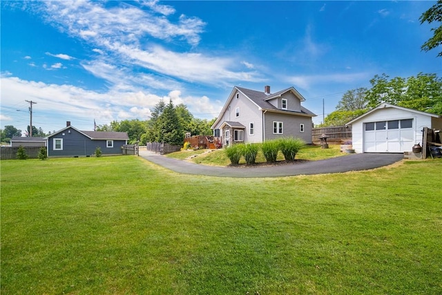 view of side of property with aphalt driveway, fence, a lawn, an outbuilding, and a detached garage