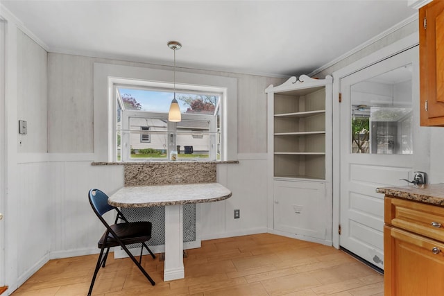 dining space featuring a decorative wall, ornamental molding, wainscoting, and light wood-type flooring