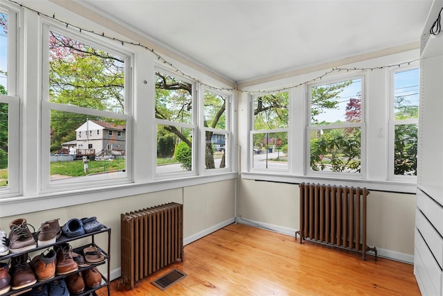 unfurnished sunroom with radiator heating unit, wood finished floors, and visible vents