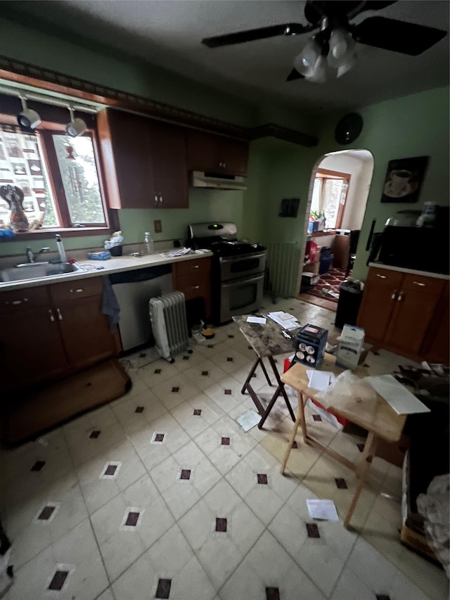 kitchen with appliances with stainless steel finishes, a sink, arched walkways, a ceiling fan, and under cabinet range hood