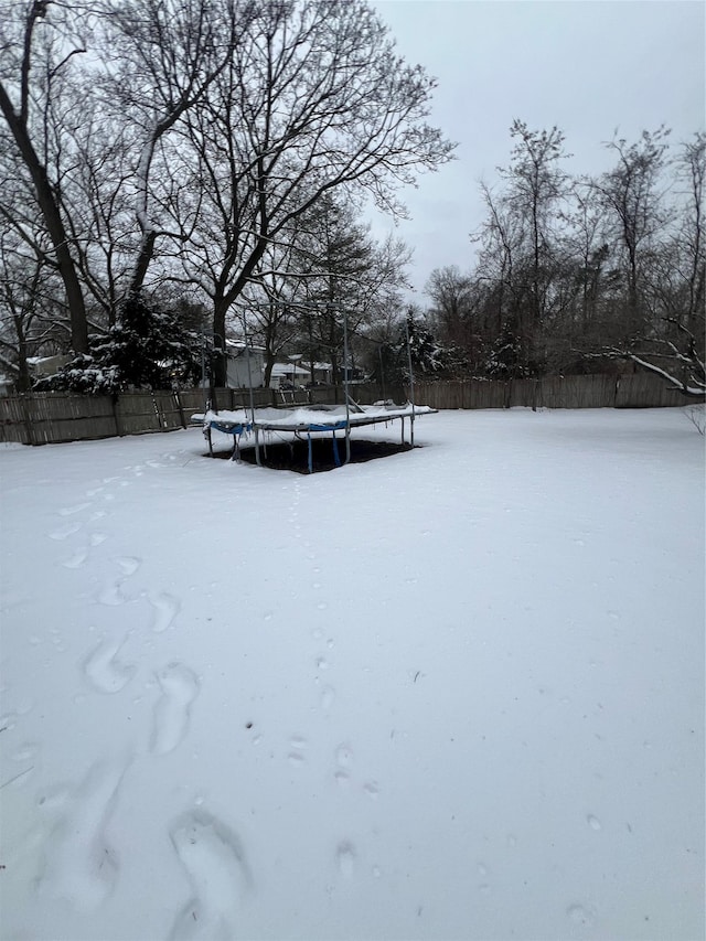 yard layered in snow with a fenced backyard and a trampoline
