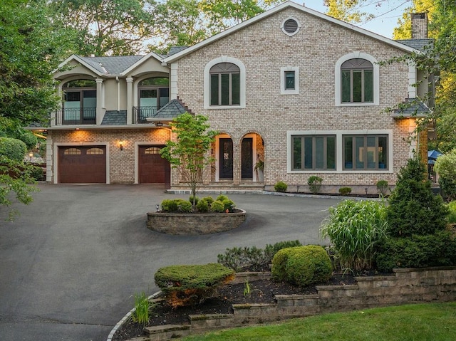 view of front facade featuring an attached garage, aphalt driveway, a balcony, and brick siding
