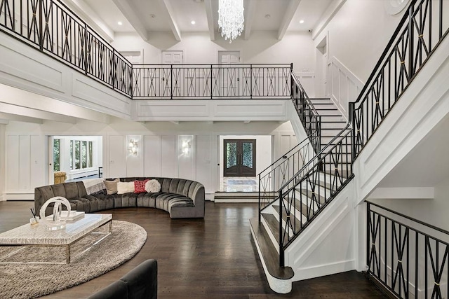 living room featuring dark wood-style flooring, a decorative wall, a high ceiling, a baseboard heating unit, and a chandelier