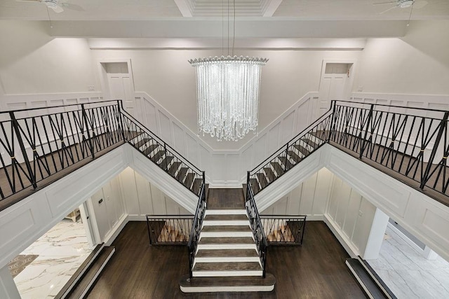 staircase with wainscoting, wood finished floors, ceiling fan with notable chandelier, and a decorative wall