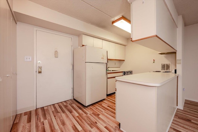 kitchen with freestanding refrigerator, light countertops, light wood finished floors, and a peninsula