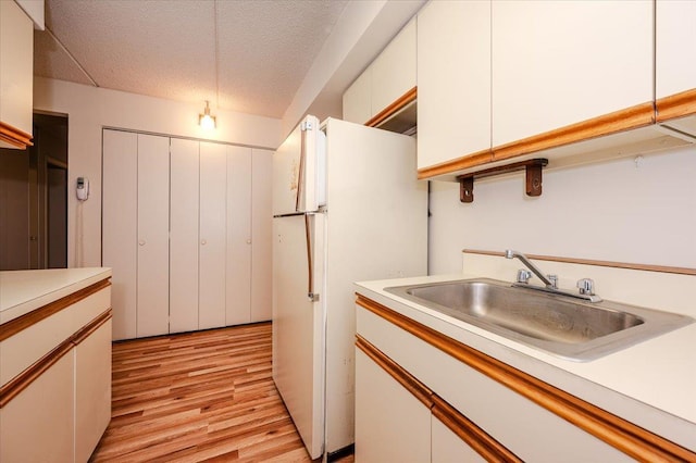 kitchen with freestanding refrigerator, light countertops, light wood-type flooring, and a sink