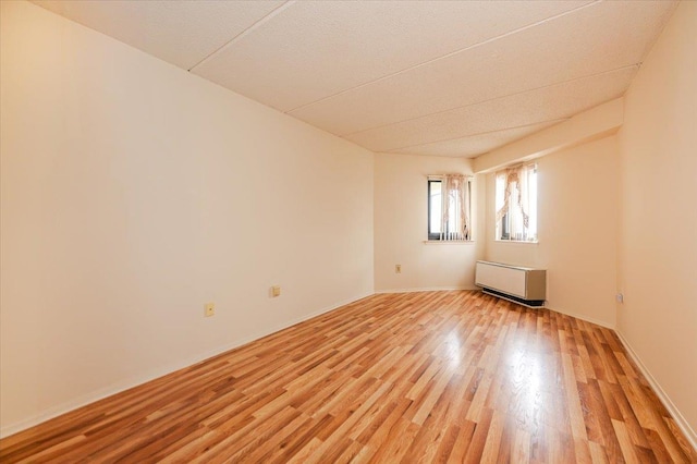 unfurnished room with radiator, baseboards, and light wood-style floors