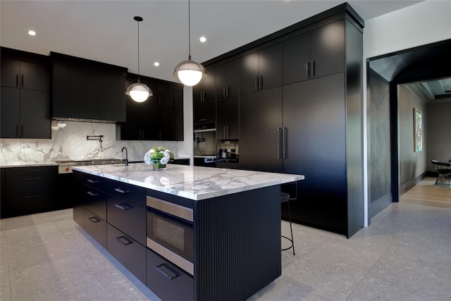 kitchen with pendant lighting, light stone counters, a breakfast bar area, tasteful backsplash, and dark cabinets