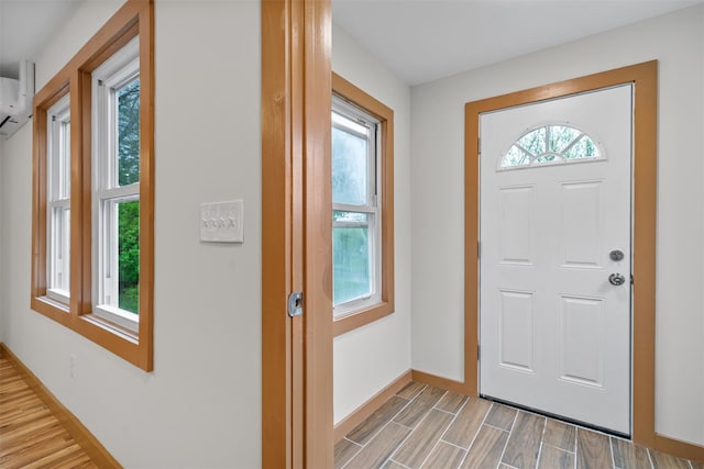 entrance foyer featuring light wood-style floors, baseboards, and an AC wall unit